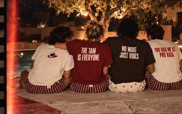 Four friends sitting shoulder to shoulder at the edge of a pool, facing the water