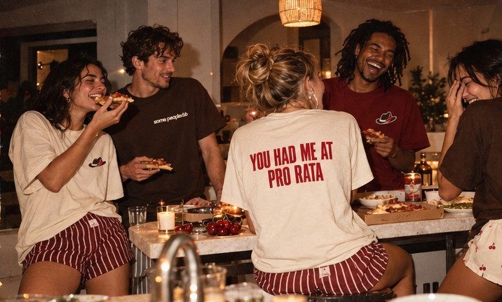 Friends sharing pizza around a marble island at night, one wearing a 'you had me at pro rata' tee
